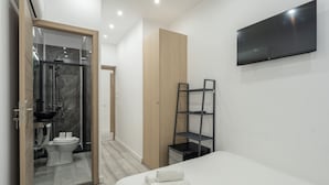 Una habitación de hotel moderna con ducha, inodoro, cama y televisor montado.