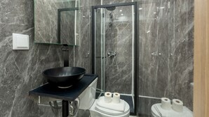 Un baño moderno con cabina de ducha de vidrio, un lavabo negro y dos inodoros.