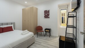 A bedroom with a bed, a wardrobe, a chair, a small table, a TV, and a window. - Lisbon Modern Suites III by Homing (Lisbon)