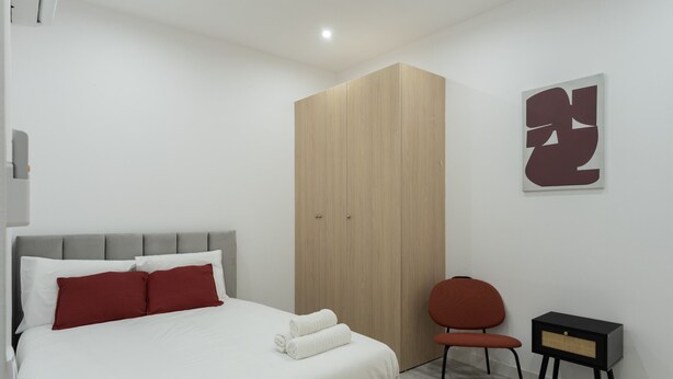 A modern hotel room with a bed, a wardrobe, a chair, and a small table. - Lisbon Modern Suites III by Homing (Lisbon)