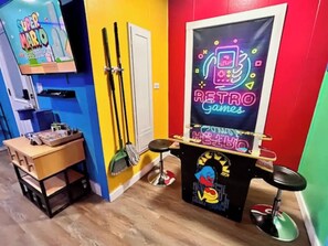 A colorful room with a retro games poster, a broom, and a desk with items on it. - GameZone PacMan Arcade, WiFi, Free Parking (Sparks)
