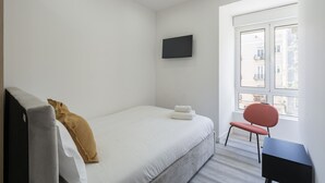 Une chambre à coucher avec un lit, une chaise, un téléviseur et une fenêtre.