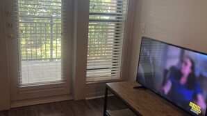 Een kamer met een houten vloer, een tv op een standaard en een deur met zonwering.