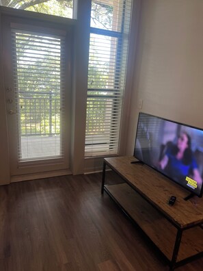 Ein Zimmer mit Holzboden, einem Fernseher auf einem Schrank und einer Tür mit Jalousien.