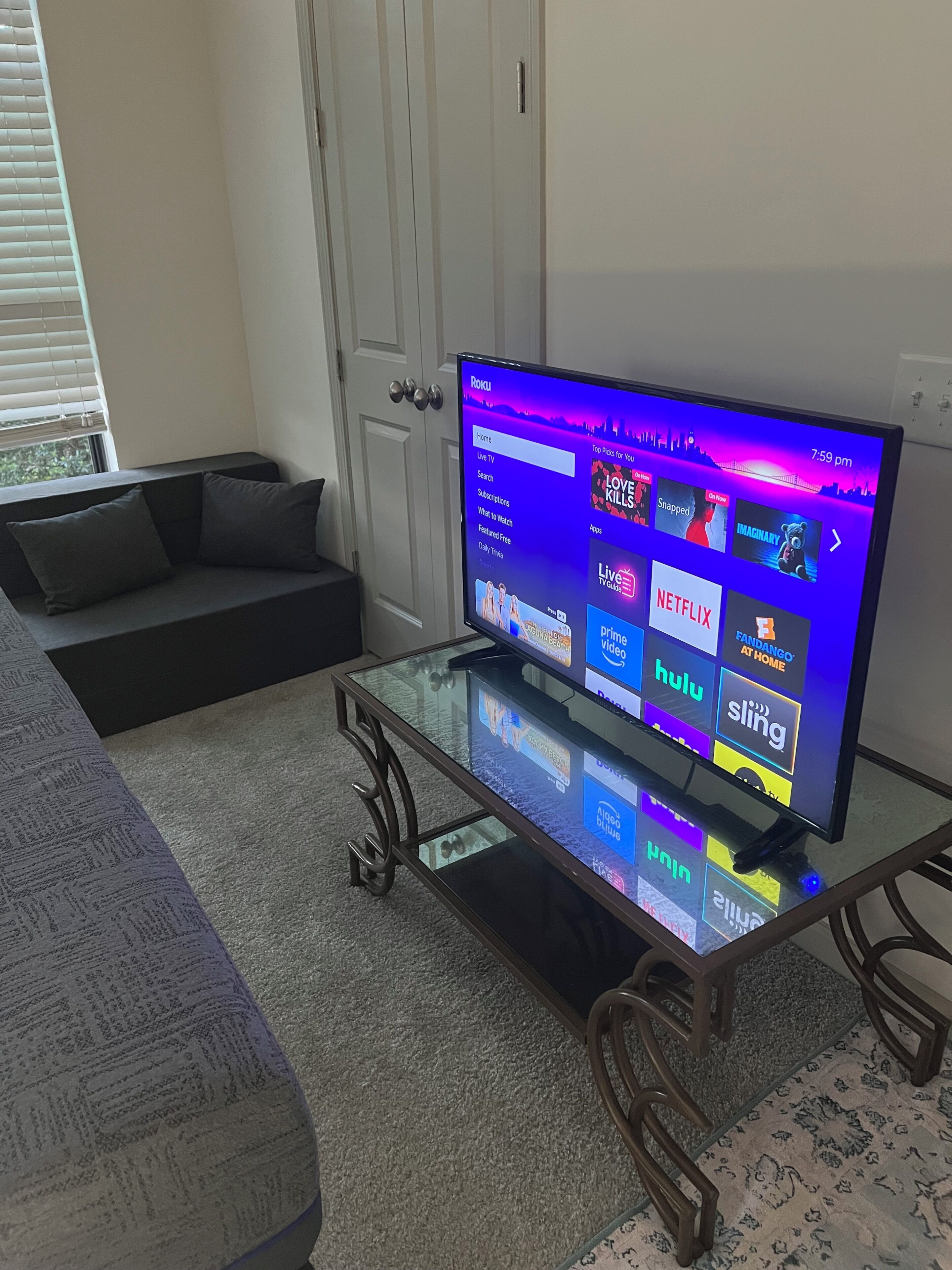 A living room with a glass-top coffee table, a sofa, and a television displaying a streaming service interface.