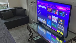 Een woonkamer met een glazen salontafel, een bank en een televisie waarop een streamingdienst wordt weergegeven.