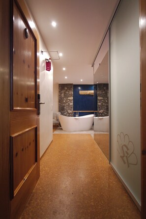 Un baño moderno con pared de piedra, una bañera blanca y un espejo grande.