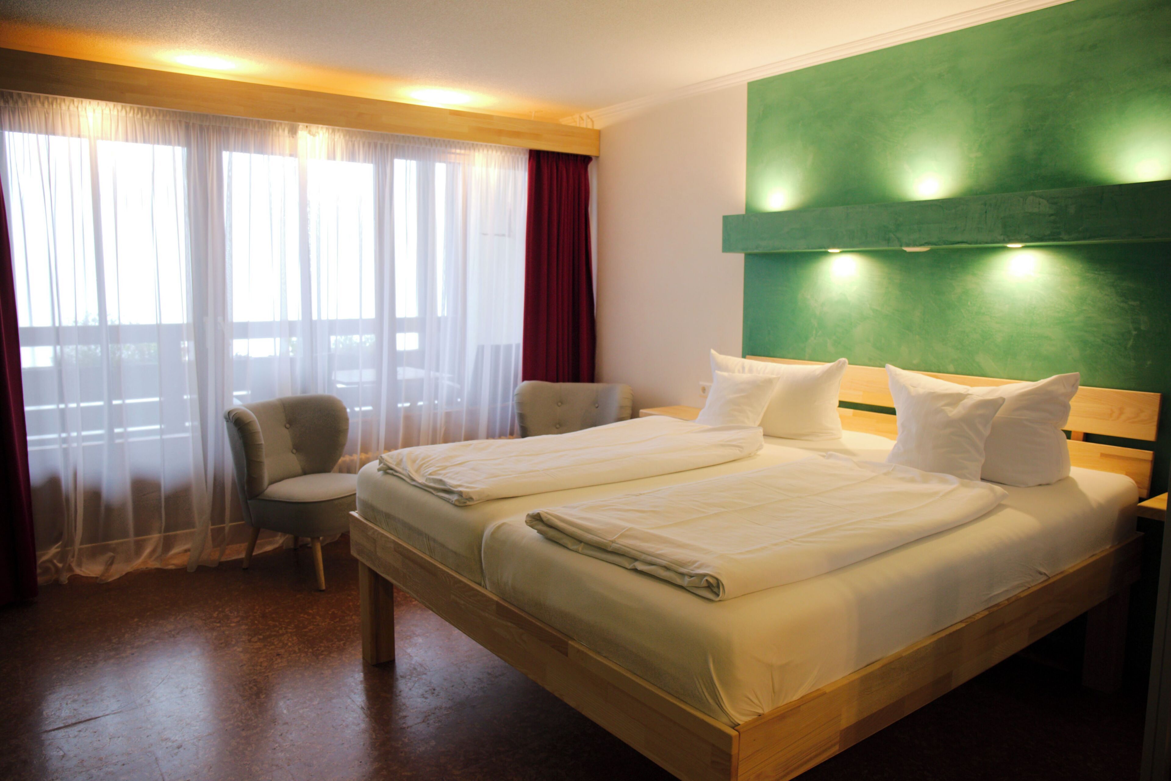 A hotel room with two beds, a chair, and a green accent wall.