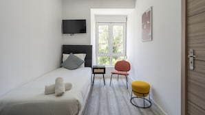 Ein modernes Hotelzimmer mit Bett, Fernseher, Fenster, Stuhl und kleinem Tisch.