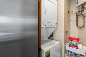 Ein Waschraum mit einer Frontlader-Waschmaschine und einem Trockner, einem Ablagefach mit Waschmittel und Kupferrohren an der Wand.