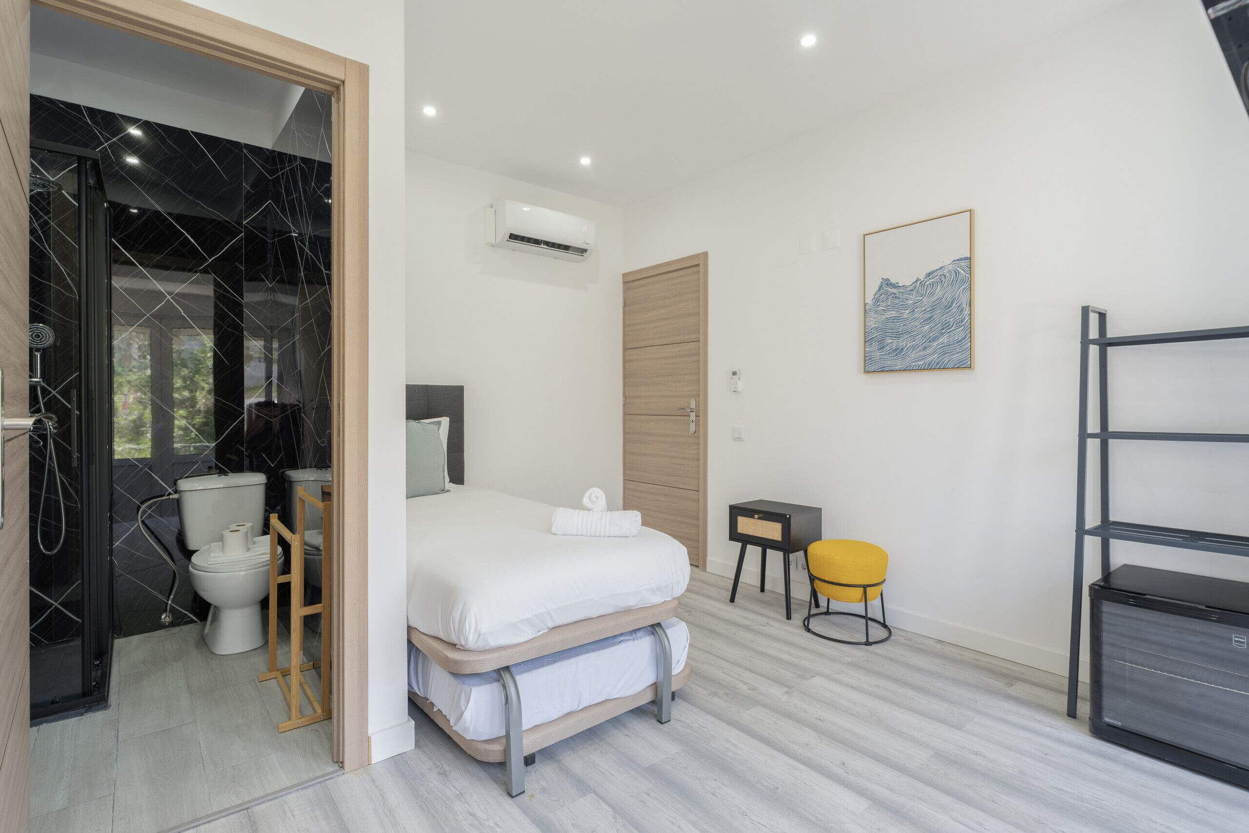 A modern bedroom with a bed, bedside table, and a small stool.