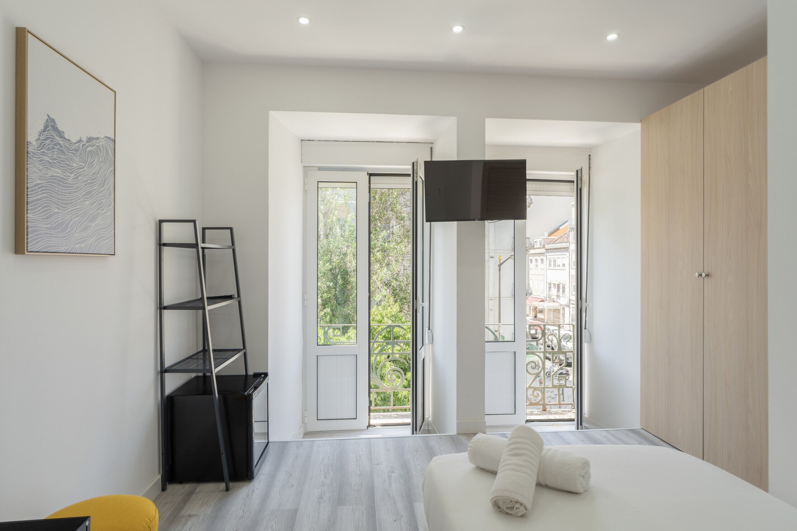 A modern bedroom with a bed, a TV, a balcony with a view, and a painting on the wall.