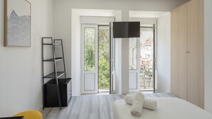 Ein modernes Schlafzimmer mit Bett, Fernseher, einem Balkon mit Blick und einem Gemälde an der Wand.