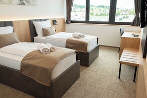 A hotel room with two beds, a desk, and a view of a town through the window.