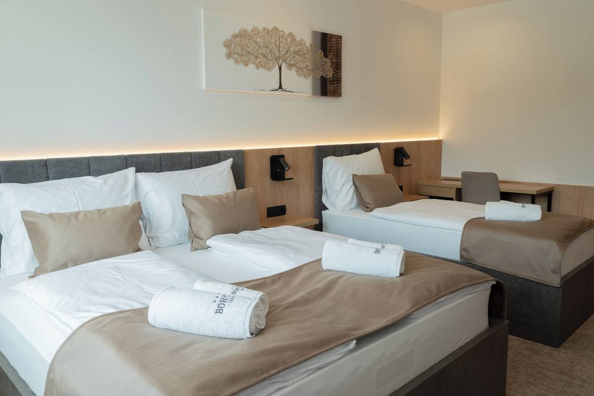 A hotel room with two beds, a desk, and a wall-mounted artwork.