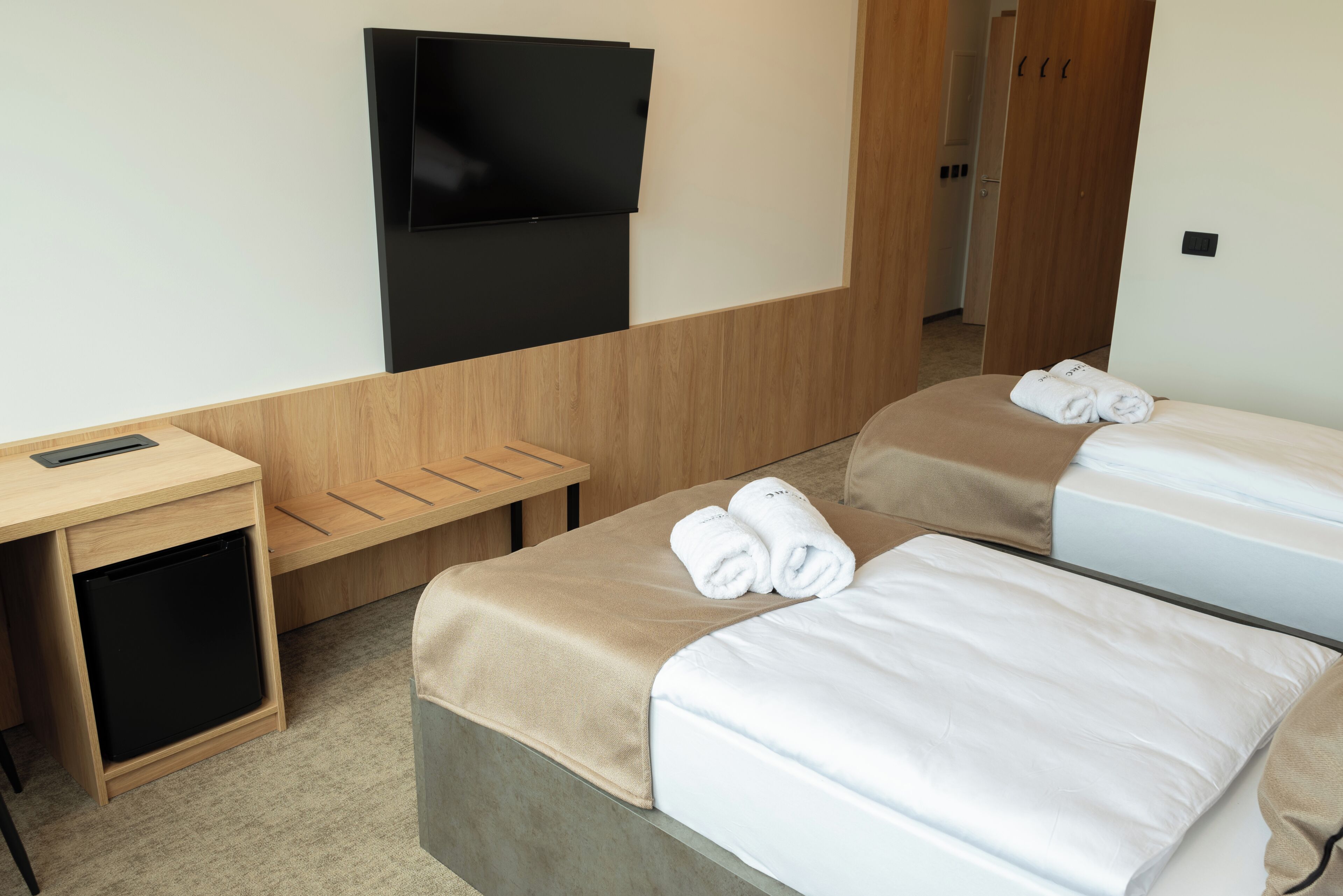 Quarto de hotel com uma cama, televisão na parede, escrivaninha e um pequeno armário.