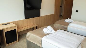 Quarto de hotel com uma cama, televisão na parede, escrivaninha e um pequeno armário.