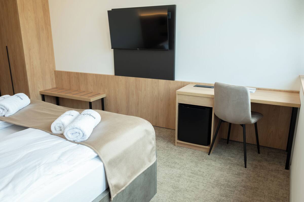 A hotel room with a bed, a desk, a chair, a TV, and a small cabinet.