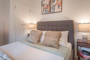 Una camera da letto con un letto, due abat-jour, un comodino con lampada e arte astratta appesa al muro.