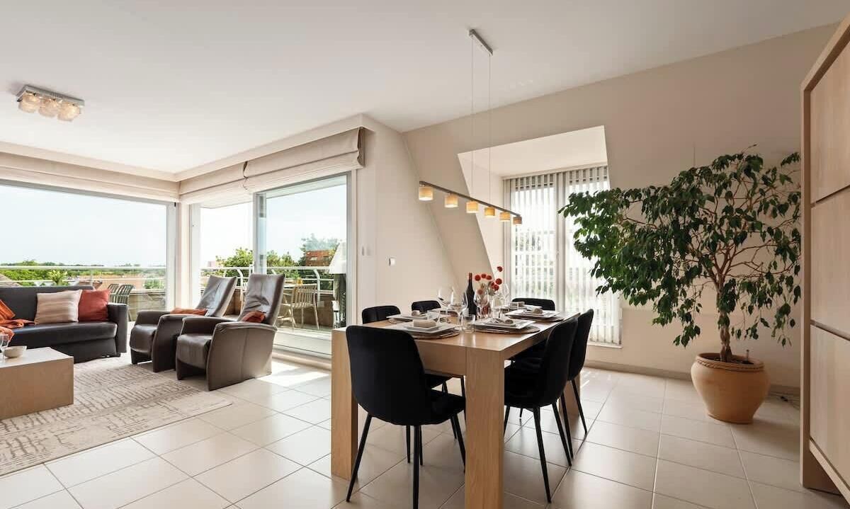 A modern living room with a dining area, large windows, and a potted plant.