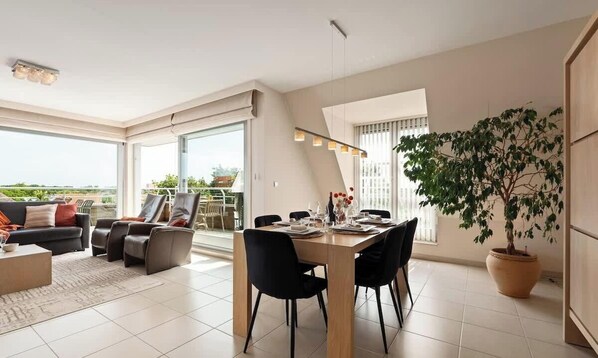 A modern living room with a dining area, large windows, and a potted plant. - Sunny Horizon - centrally located in Nieuwpoort (Nieuwpoort)