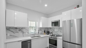 A modern kitchen with white cabinets, a stainless steel refrigerator, a microwave, a stove, and a dishwasher. - Hyde Park 1/1 private residence 8 (Tampa)