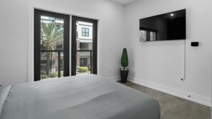 A modern bedroom with a large bed, a TV mounted on the wall, and a sliding glass door leading to an outdoor area. - Hyde Park 1/1 private residence 8 (Tampa)