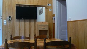 A dining area with a wooden wall, a television mounted above a table, and a door leading to another room. - Apartment 'Villa Des Familles - Aldebaran' with Mountain View, Shared Garden and Wi-Fi (La Bourboule)