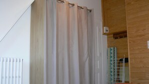 A bedroom with a bed, a curtain, a radiator, and wooden paneling. - Apartment 'Villa Des Familles - Aldebaran' with Mountain View, Shared Garden and Wi-Fi (La Bourboule)