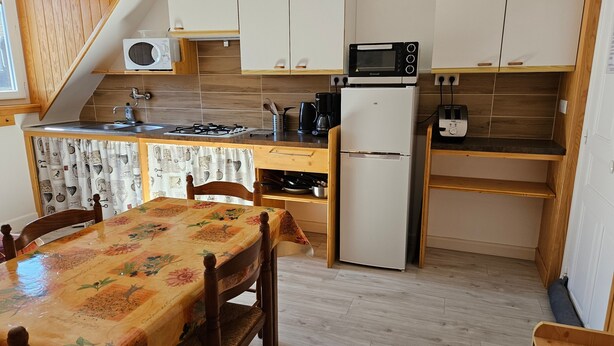 A kitchen with wooden cabinets, a microwave, a refrigerator, a stove, and a table with a floral tablecloth. - Apartment 'Villa Des Familles - Aldebaran' with Mountain View, Shared Garden and Wi-Fi (La Bourboule)