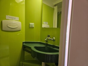 Ett badrum med en grön vägg, en vit tvåldispenser, en spegel och ett handfat med blandare.