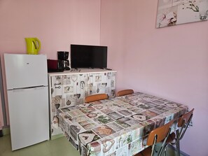 Ett litet pentry med ett kylskåp, en kaffebryggare och en platt-TV placerad ovanpå ett vitt skåp.