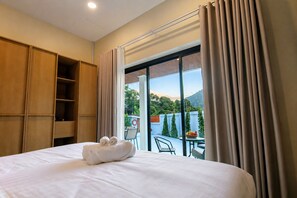 Ein Hotelzimmer mit Bett, einem Holzschrank, einem Balkon mit Tisch und Stühlen sowie Blick auf Grünflächen und Berge.