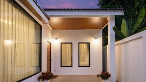 Una entrada de casa moderna con una puerta de madera, dos ventanas enmarcadas y unos pequeños escalones que llevan a la puerta.