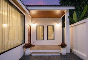 Ein moderner Hauseingang mit einer Holztür, zwei Fenster mit Rahmen und ein paar Stufen zum Eingang.