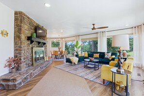 A spacious living area with a stone fireplace, a green sofa, yellow chairs, and a dining table. - The Back Nine is your Hot Springs golf course getaway! (Hot Springs)