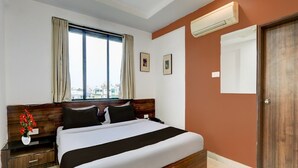 Ein Schlafzimmer mit Bett, Nachttisch, Blumen in einer Vase, einem Fenster mit Vorhängen und einer Klimaanlage.