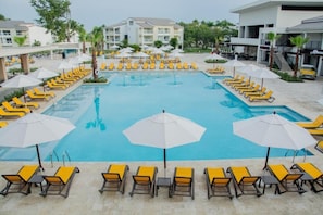 A swimming pool with sun loungers and umbrellas, surrounded by a building with multiple floors and balconies. - Hodelpa Emotions Puerto Plata (Puerto Plata)