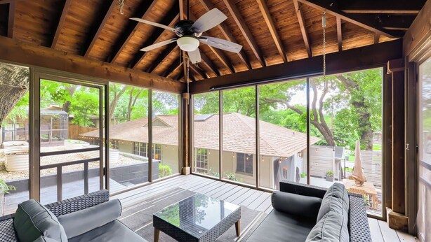 A covered outdoor seating area with a ceiling fan, a glass table, and a sofa. - Urban House in the Trees (Dallas)