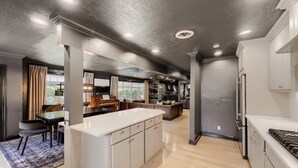 A modern kitchen with a central island, built-in appliances, and a dining area with a piano. - Urban House in the Trees (Dallas)