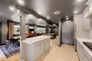 A modern kitchen with a central island, built-in appliances, and a dining area with a piano. - Urban House in the Trees (Dallas)