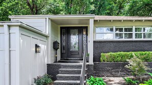 A house with a front porch, a black door, and a stone staircase leading to the entrance. - Urban House in the Trees (Dallas)