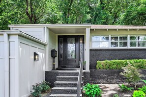 A house with a front porch, a black door, and a stone staircase leading to the entrance. - Urban House in the Trees (Dallas)