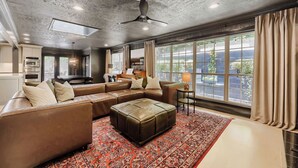A spacious living room with a large sectional sofa, a small ottoman, a piano, and a dining area. - Urban House in the Trees (Dallas)