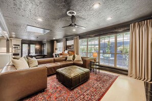 A spacious living room with a large sectional sofa, a small ottoman, a piano, and a dining area. - Urban House in the Trees (Dallas)