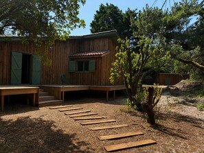 A wooden cabin with a covered porch, a small window, and a door with shutters. - House at the Foot of the Dune (Lège-Cap-Ferret)
