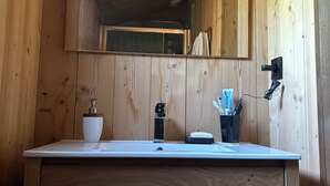 Ein Holzhäuschen im Inneren mit einem Holzwaschtisch, einem Spiegel, einem Waschbecken und einer Zahnbürstenhalterung.