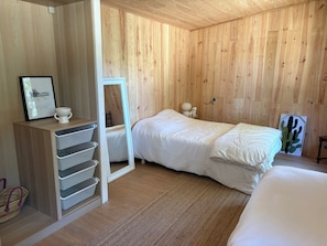 A wooden-paneled room with a bed, a mirror, a small table with a lamp, and a picture frame. - House at the Foot of the Dune (Lège-Cap-Ferret)