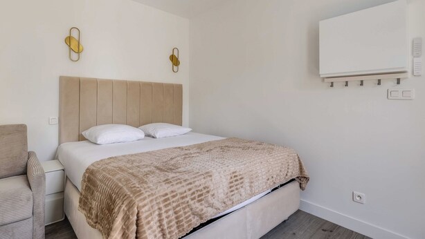 Un dormitorio con cama, una silla, aire acondicionado instalado en la pared y una pizarra.