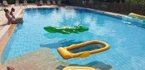 A swimming pool with two people sitting on the edge, a green inflatable crocodile float, and a yellow inflatable pool noodle. - 2 Bedroom Apartment, Balconies & Pool - Apt 3 (Kontokali)